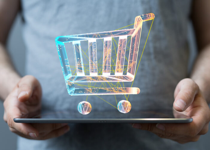 A person holding a tablet projects a glowing digital shopping cart made of interconnected neon lines and data nodes.