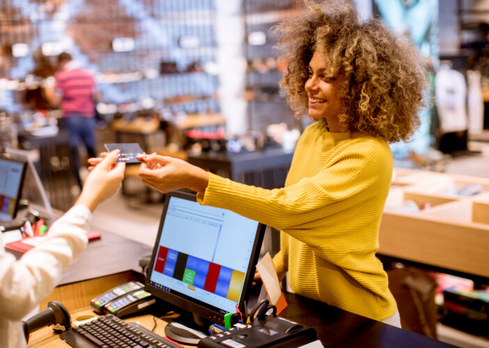 Retail associate smiling while processing a card payment at the checkout counter, supported by secure, integrated store network systems.