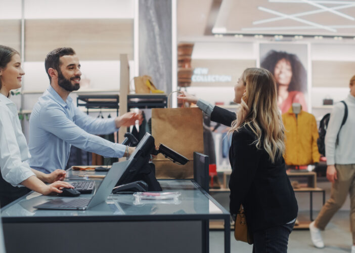 Retail staff assisting a customer at the checkout counter, representing trust and business continuity in the face of cybersecurity threats.